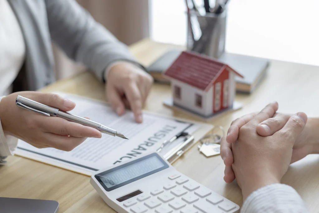 Hands, paperwork, mini house, and calculator on table
