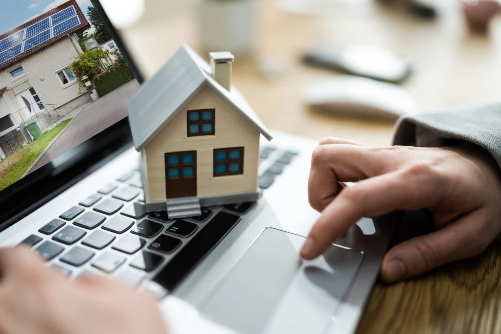 Image with mini house on laptop and hand on trackpad