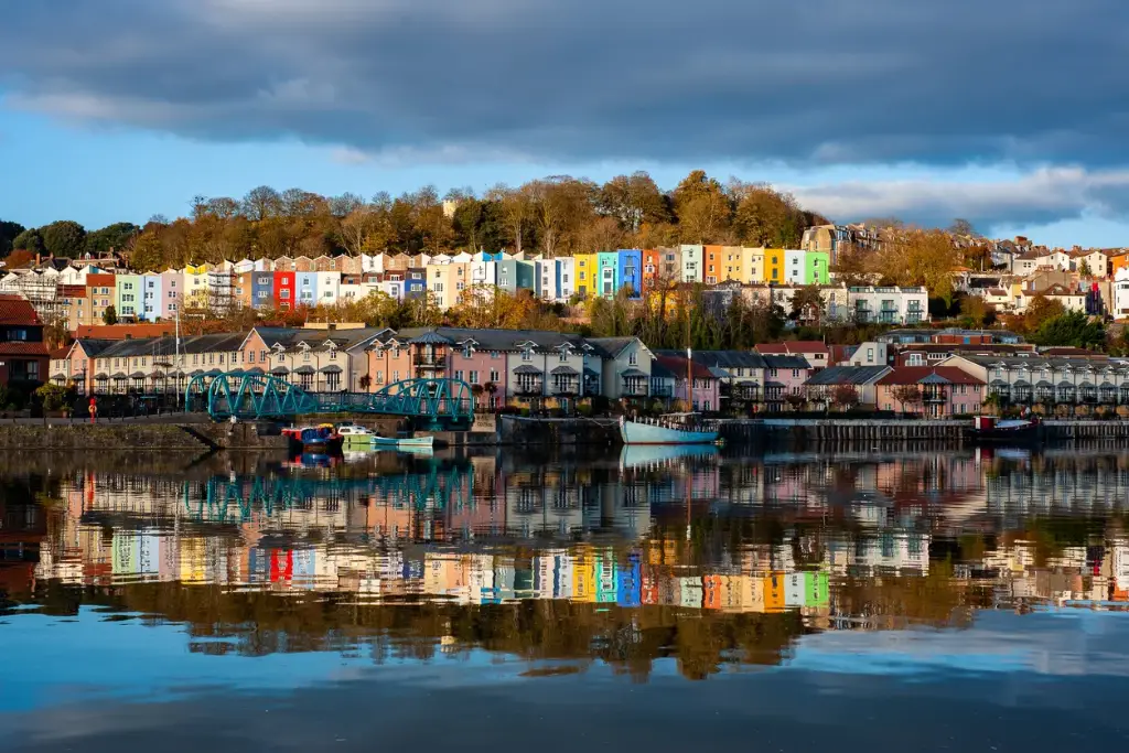 Colorful houses reflected in water at Bristol Harbourside with boats and bridge