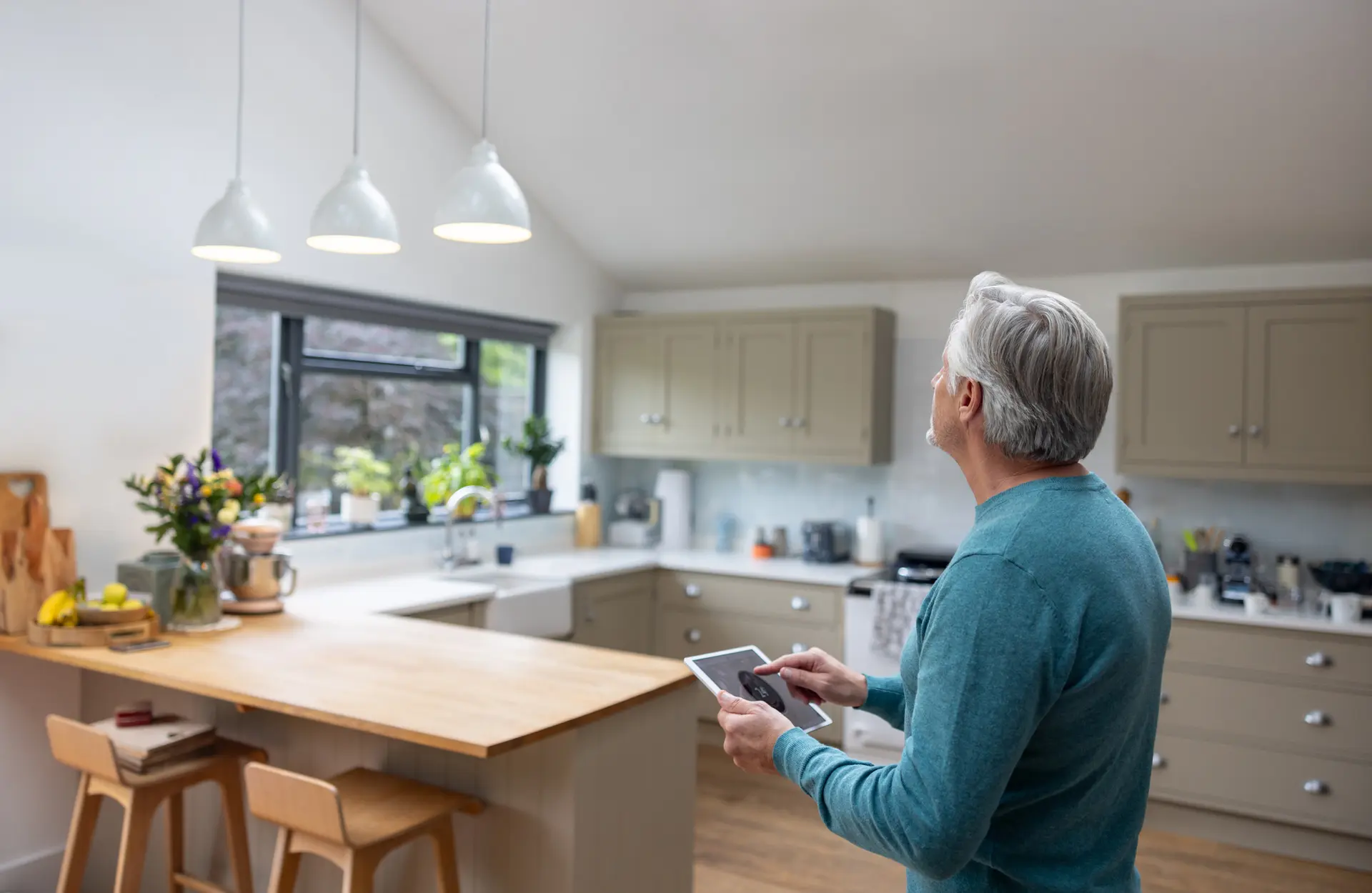 An older man standing in his kitchen using a tablet device.